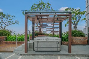 A modern outdoor seating area with a metal pergola structure, a cushioned bench, and a small table. - Ardana by Kozystay - Tunjungan (Surabaya)