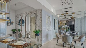 A modern dining area with a glass table, chairs, and a kitchen in the background. - Ardana by Kozystay - Tunjungan (Surabaya)