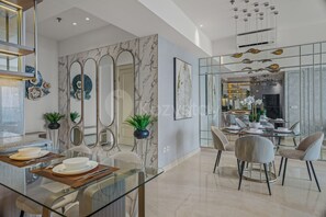 A modern dining area with a glass table, chairs, and a kitchen in the background. - Ardana by Kozystay - Tunjungan (Surabaya)