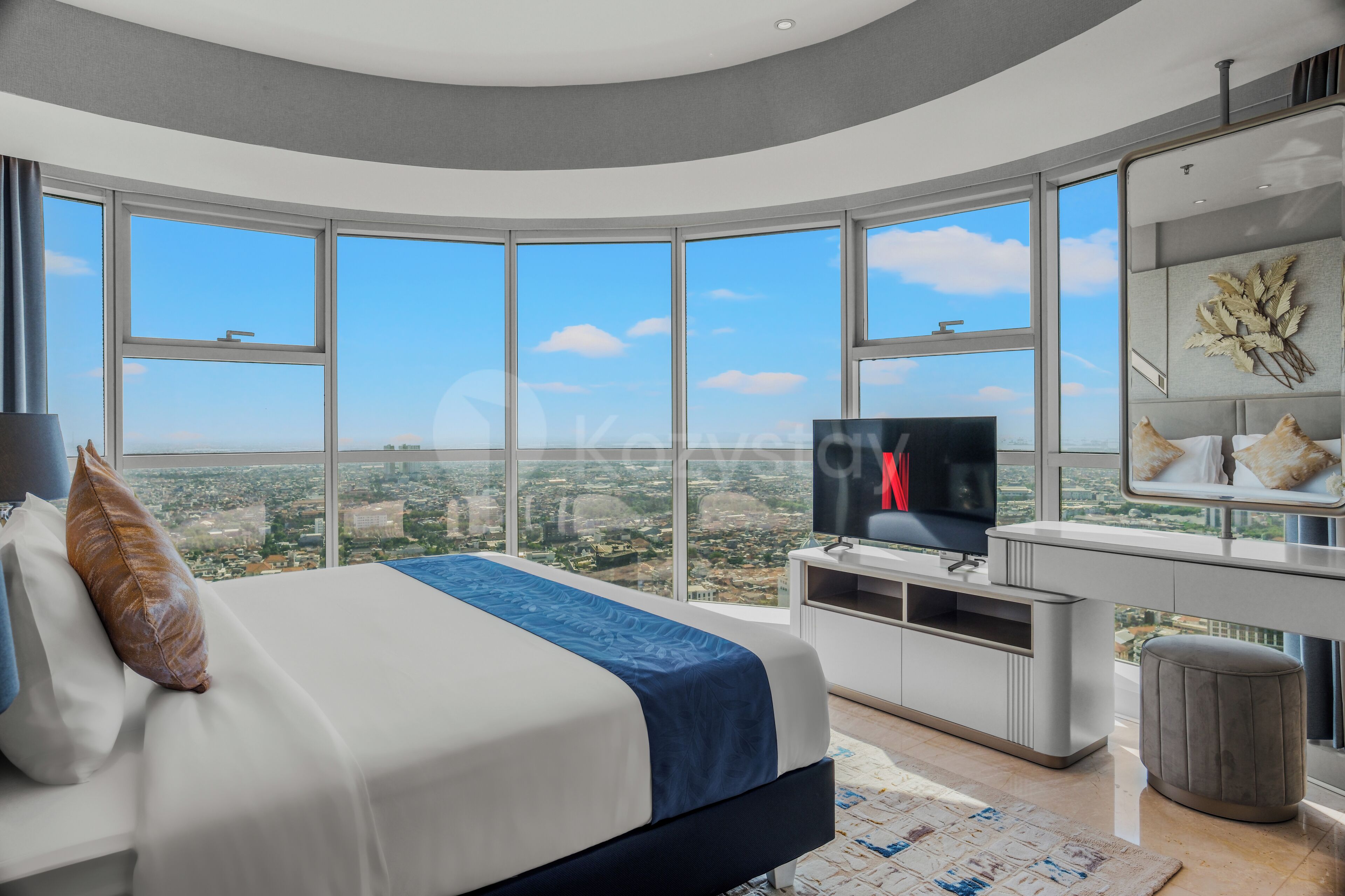 A modern bedroom with a large bed, a TV, and a desk with a view of the city.