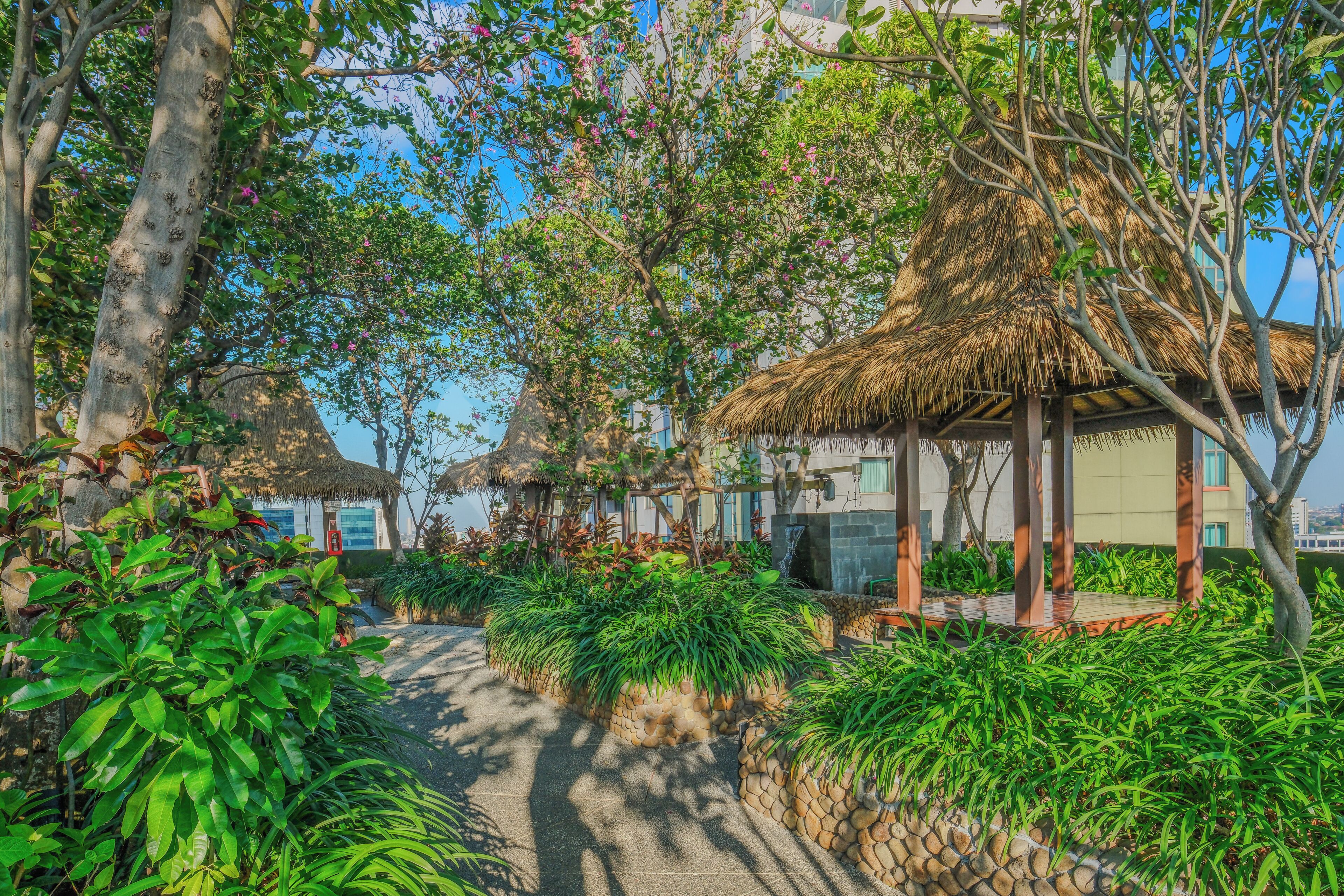 A garden area with a thatched-roof gazebo, lush greenery, and a paved pathway.