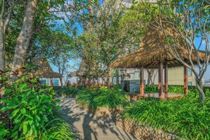 A garden area with a thatched-roof gazebo, lush greenery, and a paved pathway. - Ardana by Kozystay - Tunjungan (Surabaya)