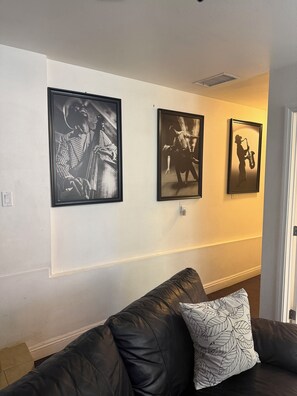 Ein Wohnzimmer mit einem schwarzen Ledersofa, einem gemusterten Kissen und drei gerahmten Schwarz-Weiß-Fotos an der Wand.