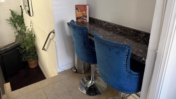 Uma cozinha com bancada de mármore, duas cadeiras estofadas em azul, uma planta em vaso e um livro de receitas sobre a bancada.