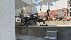 Um pátio externo com mesa e cadeiras, um degrau de concreto e um muro de tijolos.