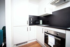Eine kleine Küche mit weißen Schränken, einer schwarzen Arbeitsplatte, einer Mikrowelle und einem Edelstahlbackofen.