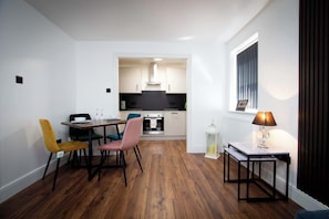 Eine kompakte Küche mit modernen Geräten, ein Essbereich mit unterschiedlichen Stühlen und ein kleiner Tisch mit einer Lampe.