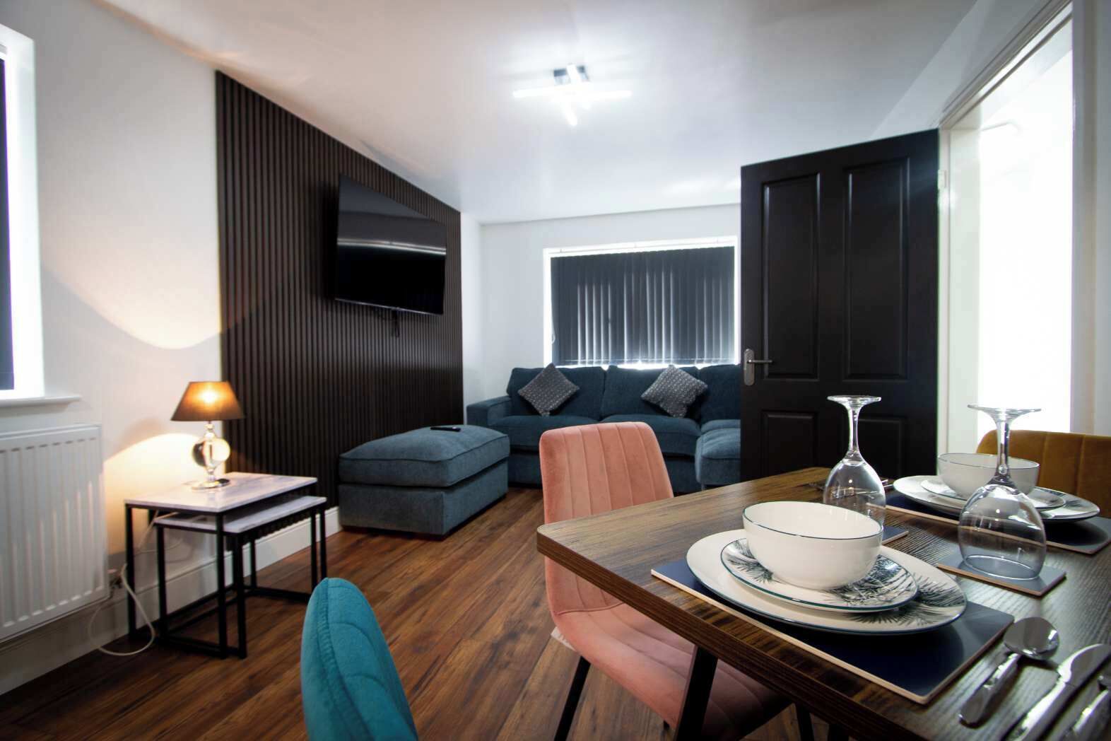 A modern living room with a sofa, a dining table set for two, and a television mounted on the wall.