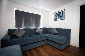 Ein modernes Wohnzimmer mit einem Ecksofa, einem gerahmten abstrakten Gemälde und einem großen Fenster mit Jalousien.