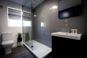 A modern bathroom with a glass shower enclosure, a toilet, a sink with a mirror, and a window providing natural light. - Stylish 2BR Flat in Tyldesley with Parking & Sleeps 4 (Tyldesley)