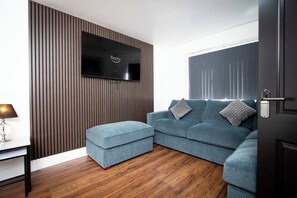 Ein modernes Wohnzimmer mit einer Eckcouch, einem Flachbildfernseher, der an einer Wand aus Holzpaneelen befestigt ist, und Holzböden.