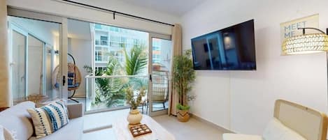 Un salon moderne avec un canapé, une table basse, un téléviseur fixé au mur et un balcon agrémenté de plantes.