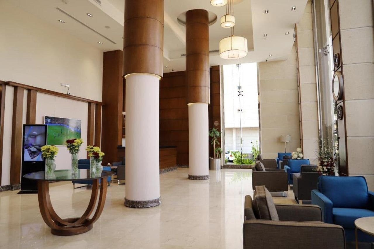 Un hall d’entrée moderne avec de hauts plafonds, de grandes colonnes et un espace détente comprenant des canapés et des fauteuils.
