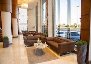 A modern lobby with a seating area, large windows, and a view of the street. - Banan Hotel (Tabuk)