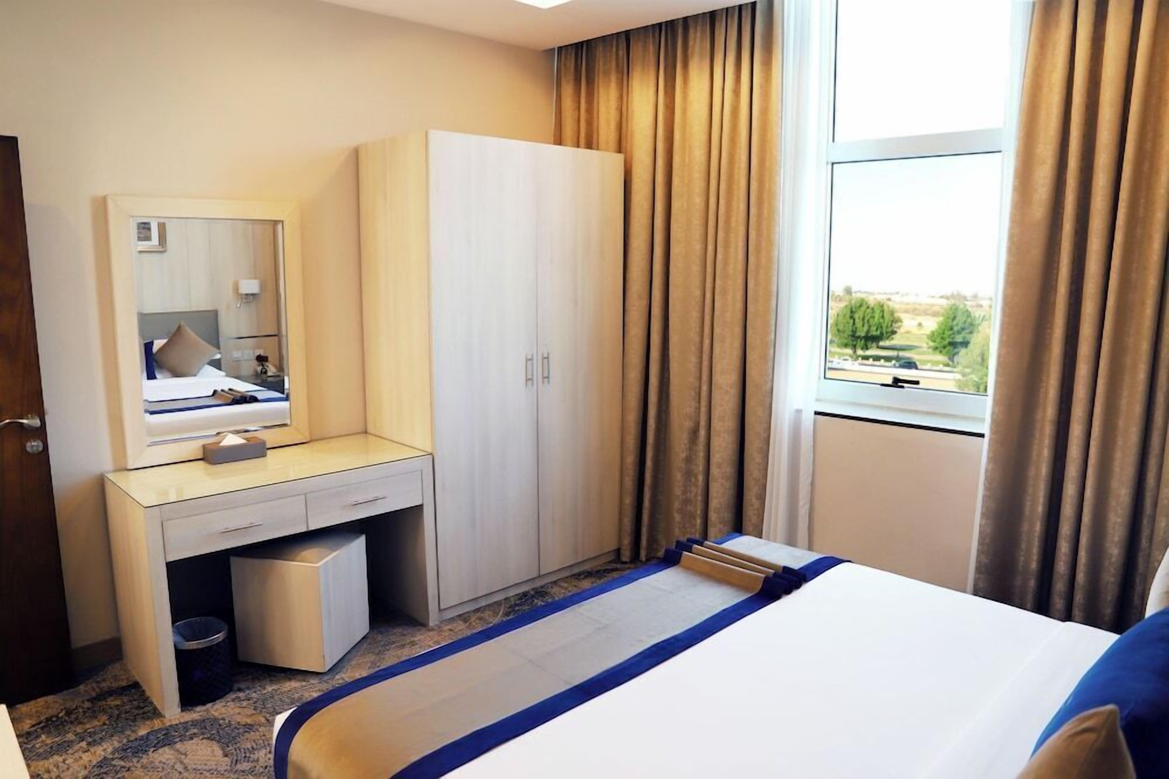 Habitación de hotel con cama, escritorio con espejo, armario y ventana con cortinas.