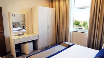 Habitación de hotel con cama, escritorio con espejo, armario y ventana con cortinas.