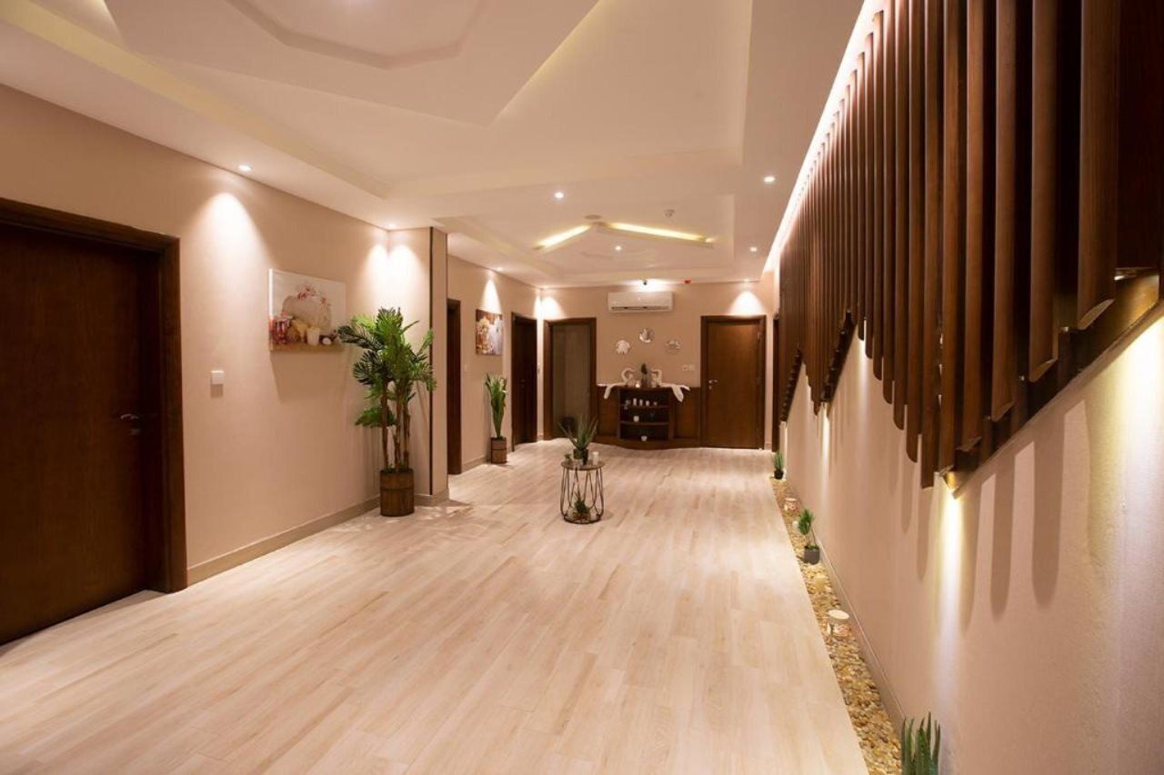 Un pasillo de hotel con suelo de madera, plantas en macetas y una zona de estar central.