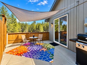 Une terrasse avec un barbecue, une table entourée de chaises et un tapis aux couleurs vives.
