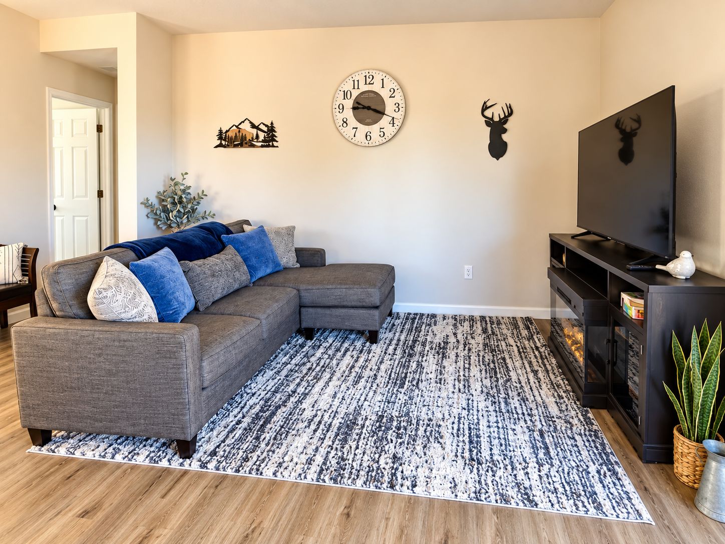 A living room with a sectional sofa, a patterned rug, a wall clock, and a mounted deer head.
