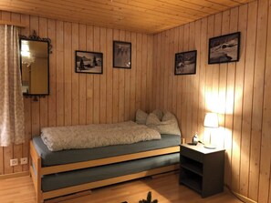 Ein Zimmer mit Holzvertäfelung, einem Bett, einem Nachttisch mit Lampe und drei gerahmten Bildern an der Wand.