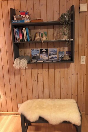 Uma estante com livros e objetos decorativos, um pequeno banco com um cobertor de pele e uma parede de madeira.