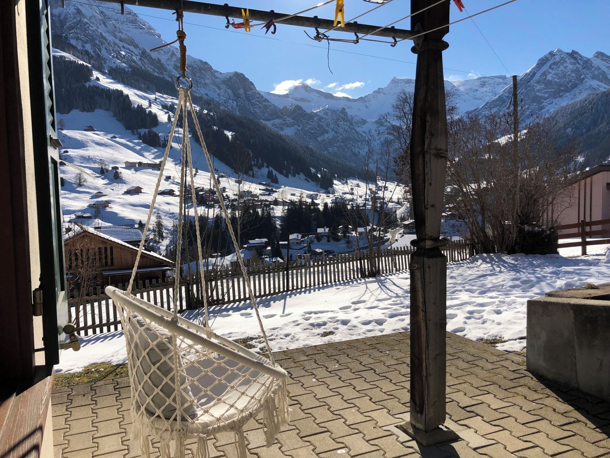 Eine Hängesessel auf einer Ziegelterrasse mit Blick auf verschneite Berge und einen Holzzaun.