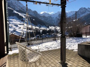 Un fauteuil suspendu sur une terrasse en briques, avec vue sur des montagnes enneigées et une clôture en bois.