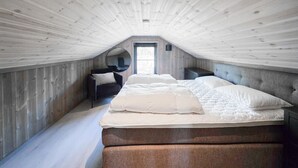 A bedroom with a sloped ceiling, a bed with white bedding, a dark armchair, and a small bedside table. - Gorgeous home in Vinje with WiFi (Vinje)