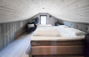 Ein Schlafzimmer mit schrägen Wänden, einem Bett mit weißer Bettwäsche, einem dunklen Sessel und einem kleinen Nachttisch.