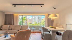 Una sala de estar moderna con sofá, sillones, una mesa de comedor y vistas a edificios a través de amplios ventanales.