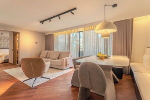 Ein modernes Wohnzimmer mit einer Couch, Sesseln, einem Esstisch und einem großen Fenster mit Vorhängen.