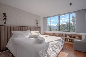Ein modernes Schlafzimmer mit einem großen Bett, Blick ins Freie und einem Holz-Kopfteil.