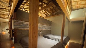 Habitación con cama, vigas de madera, techo inclinado y vistas al exterior.