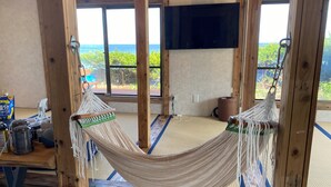 Una habitación con hamaca, vigas de madera, televisor y vista al mar.