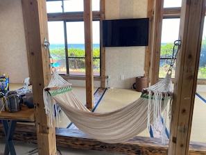 A room with a hammock, wooden beams, a television, and a view of the sea.