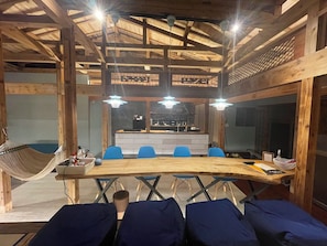 A wooden interior with a long table, blue chairs, and a hammock. - Keshiki Tamari | Open-Air Bath with Private Beach (Amami-shi)