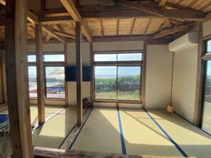 A room with tatami mat flooring, large windows with a view of the sea, and a wooden ceiling structure. - Keshiki Tamari | Open-Air Bath with Private Beach (Amami-shi)