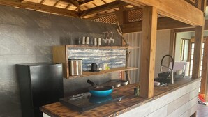 Una cocina con un refrigerador negro, una olla azul, una cafetera y un estante de madera con cristalería.