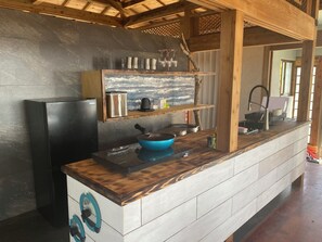 A kitchen with a black refrigerator, a blue cooking pot, a coffee maker, and a wooden shelf with glassware.