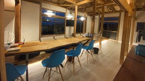Una habitación amplia con una larga mesa de madera y sillas azules, ventanas grandes y un techo alto con vigas a la vista.