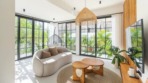 A modern living room with large windows, a sofa, a coffee table, and a hanging light fixture. - Ubud's Best 2BR w Huge Rooftop & Pool by Ricefield (Ubud)