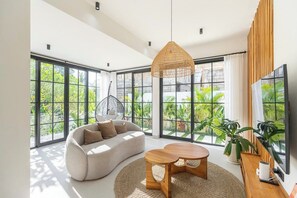 Un saló modern amb grans finestres, un sofà, una taula de centre i un llum penjant.