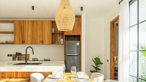 A modern kitchen with wooden cabinets, a stainless steel refrigerator, and a dining area with a wooden table and chairs. - Ubud's Best 2BR w Huge Rooftop & Pool by Ricefield (Ubud)