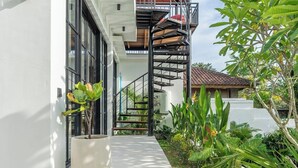 A modern building with a white exterior, a concrete staircase leading to a wooden deck, and lush greenery. - Ubud's Best 2BR w Huge Rooftop & Pool by Ricefield (Ubud)