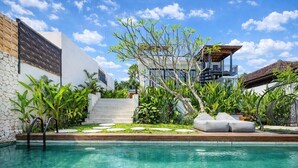 A swimming pool with a stone wall, a wooden deck, and a staircase leading to a balcony. - Ubud's Best 2BR w Huge Rooftop & Pool by Ricefield (Ubud)