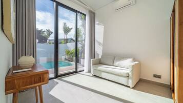 Ein modernes Wohnzimmer mit einer Couch, einem Holztisch und einer großen Schiebeglastür, die zu einem Pool führt.