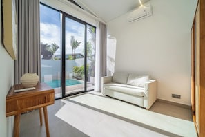 Ein modernes Wohnzimmer mit einer Couch, einem Holztisch und einer großen Schiebeglastür, die zu einem Pool führt.