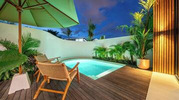 Ein Holzdeck mit einem Pool, umgeben von tropischen Pflanzen und einem grünen Sonnenschirm.