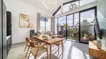 Un espace de repas moderne avec une table et des chaises en bois, un canapé et une grande fenêtre donnant sur l’extérieur.