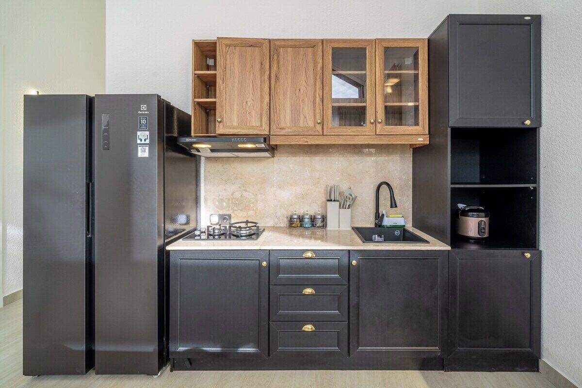 Eine kompakte Küche mit schwarzen Schränken, einem Edelstahl-Kühlschrank, einem Gasherd und einem eingebauten Backofen.
